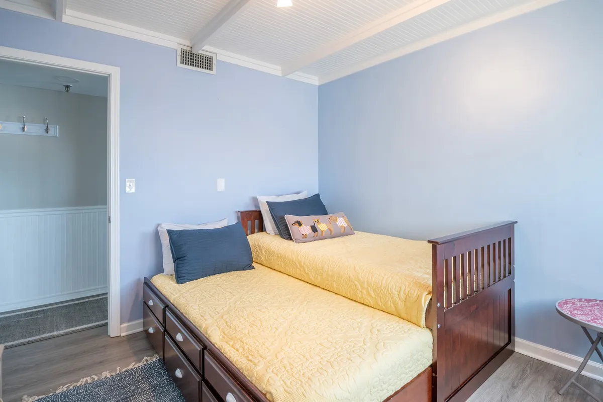 A playful and inviting bedroom featuring twin beds with decorative pillows and a bold blue accent wall. The space is designed for relaxation and sharing, ideal for children or friends.