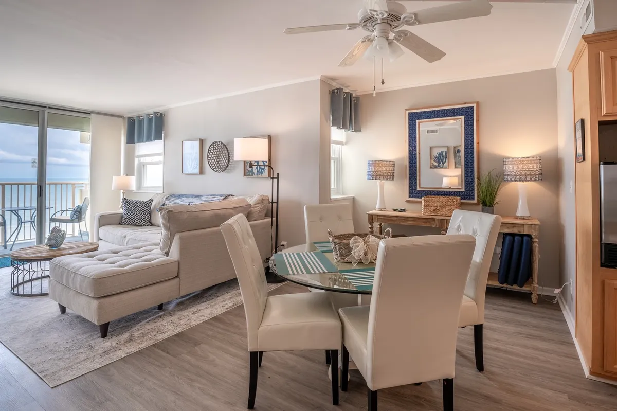 This image showcases a spacious, open-concept living and dining area featuring a comfortable sectional sofa, a dining table with striped décor, and large windows that frame stunning ocean views. Natural light fills the space, creating a relaxed and inviting atmosphere for gatherings or quiet moments.