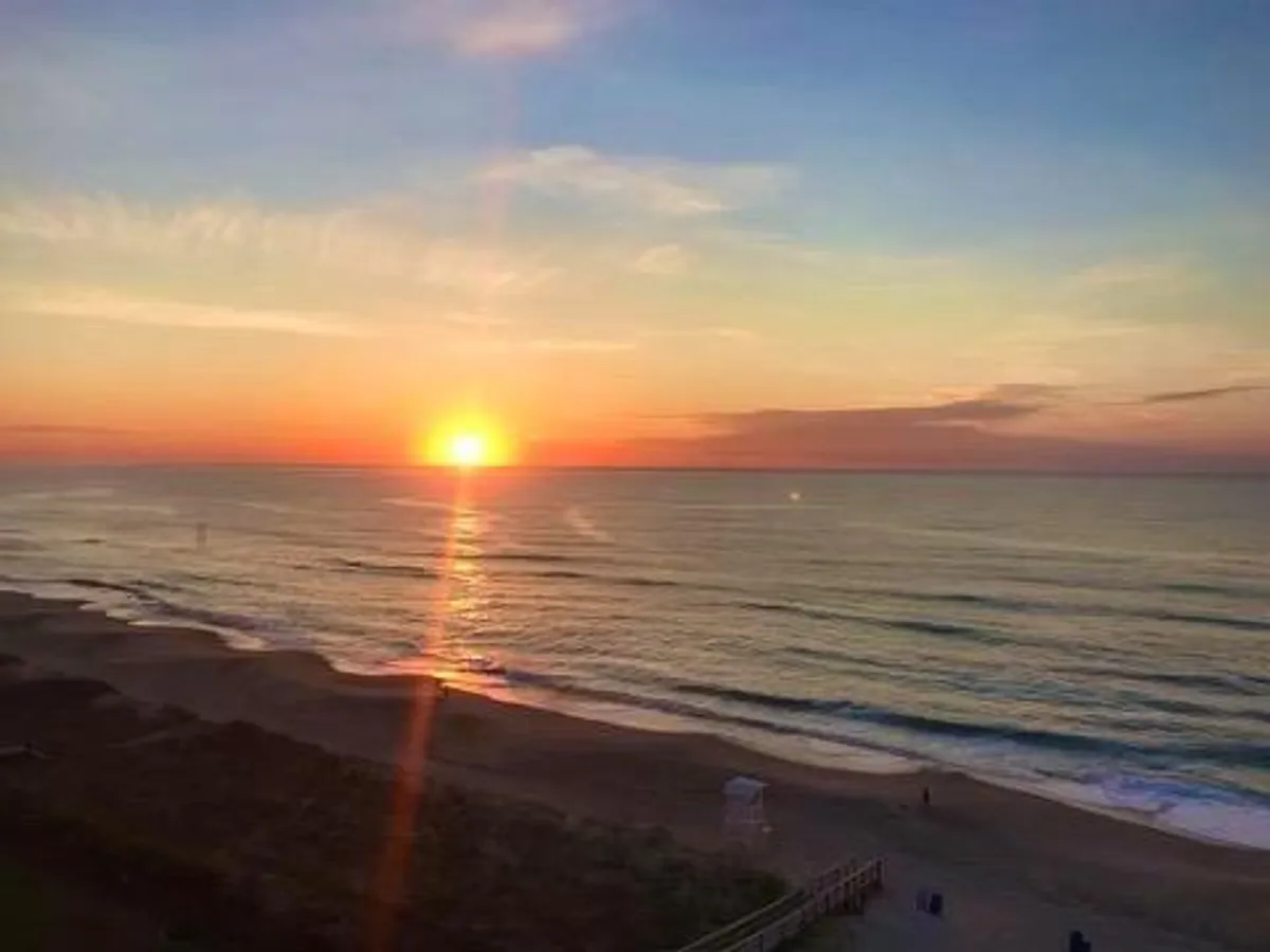 A view of the beach at sunset, with gentle ocean waves and sandy shore in the foreground. The serene setting invites moments of relaxation, beach walks, and sharing a group sunset experience.