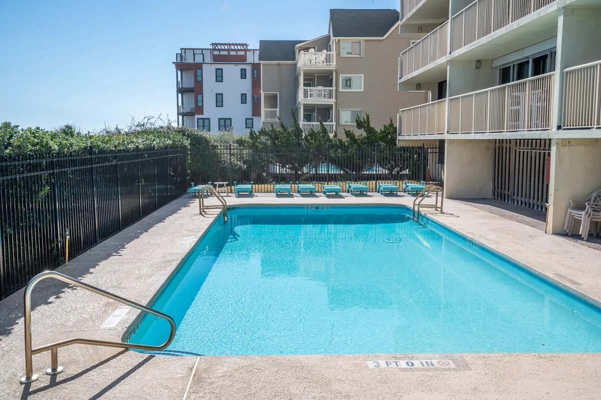 This image showcases the community's sparkling outdoor swimming pool surrounded by comfortable lounge chairs and lush greenery, inviting residents and guests to enjoy sunbathing, swimming, and relaxing outdoors. The setting is vibrant and relaxed, perfect for summer poolside gatherings and family fun days.