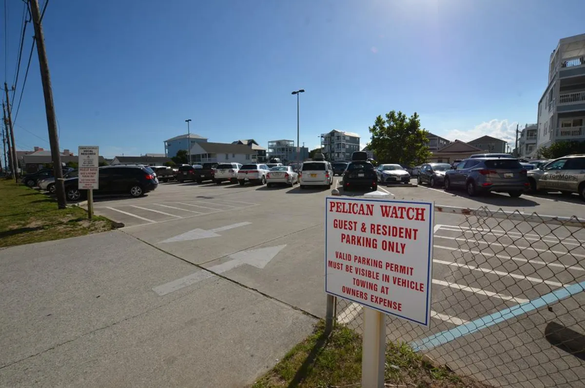 An exterior shot showing the property’s parking lot, signage, and surrounding buildings. The scene conveys a sense of arrival and community access, with guests and residents coming and going.