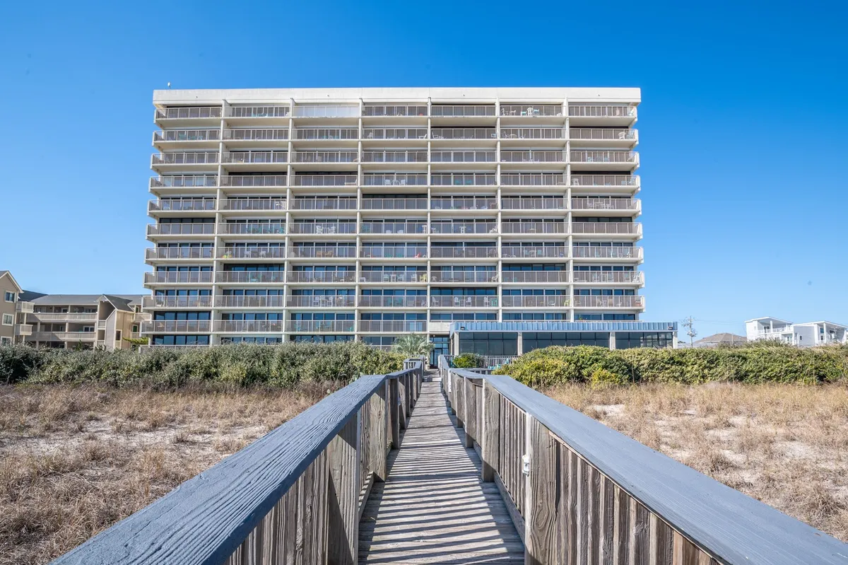 A serene exterior shot of the beachfront condominium, featuring the wooden walkway leading directly to the beach, lush surrounding vegetation, and the building’s balconies facing the ocean.