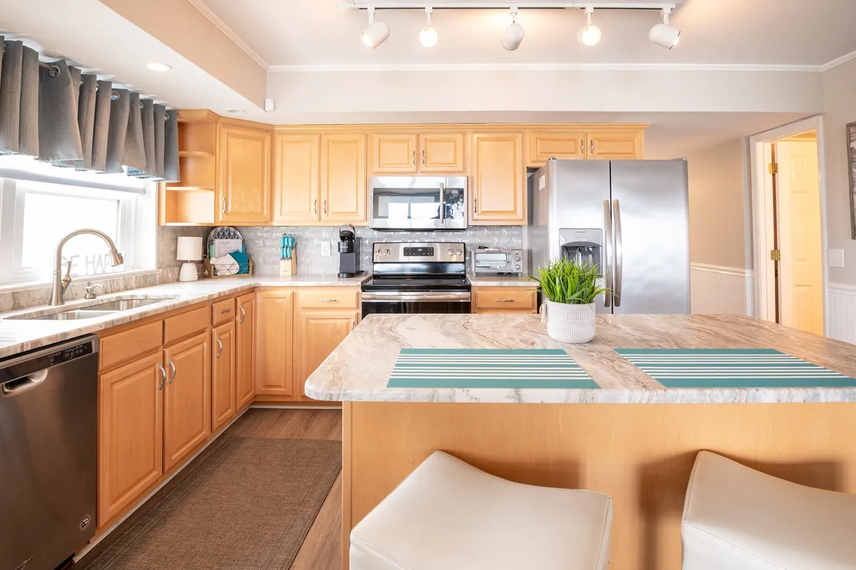 A sunlit kitchen featuring a central island, sleek stainless steel appliances, and a window that brings in plenty of natural light. High-end cabinetry and granite countertops set the stage, complemented by a decorative plant that adds a fresh, welcoming touch. The space is designed for both cooking and socializing, with clear zones for meal prep, coffee rituals, and entertaining.